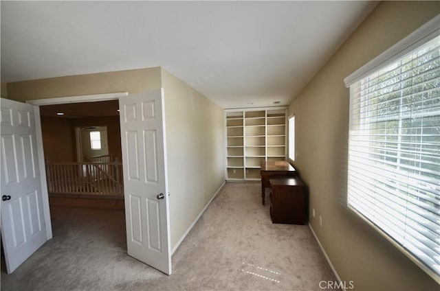 hallway with light carpet, baseboards, built in features, and an upstairs landing