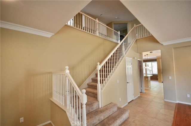 staircase featuring baseboards, crown molding, tile patterned flooring, and a high ceiling