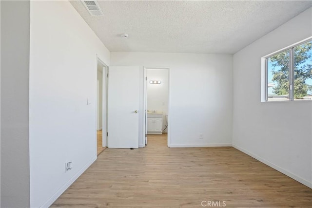 unfurnished bedroom featuring a textured ceiling, light hardwood / wood-style floors, and connected bathroom