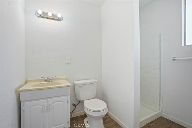 bathroom with toilet, vanity, tiled shower, and hardwood / wood-style flooring