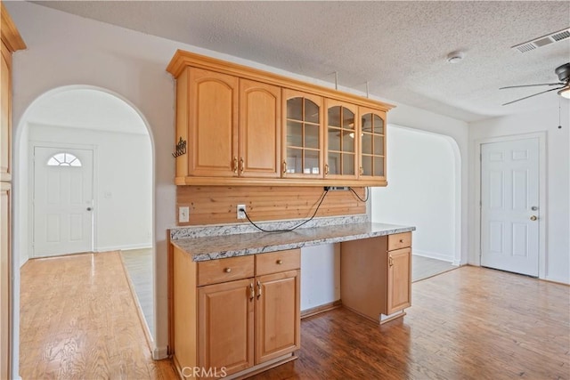 kitchen with ceiling fan, light stone countertops, a textured ceiling, and hardwood / wood-style floors