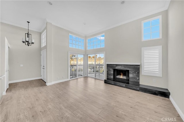 unfurnished living room with light hardwood / wood-style flooring, a towering ceiling, a chandelier, and ornamental molding