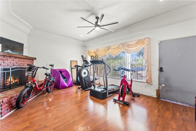 workout area with ceiling fan, a fireplace, and wood-type flooring