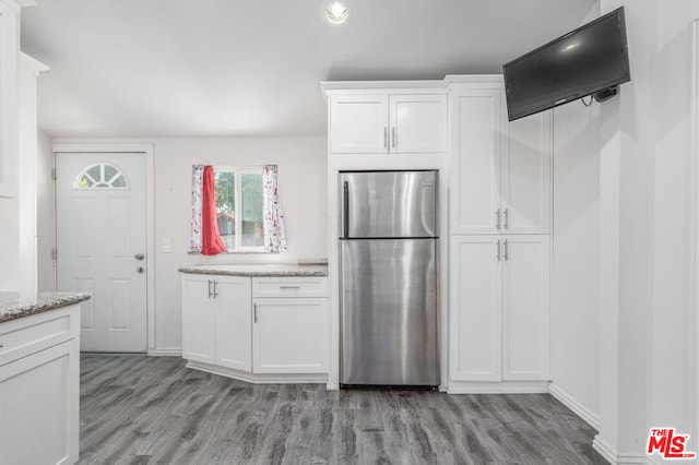 kitchen with white cabinets, stainless steel fridge, light wood-type flooring, and light stone countertops