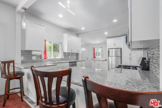 kitchen with kitchen peninsula, appliances with stainless steel finishes, decorative backsplash, sink, and white cabinetry