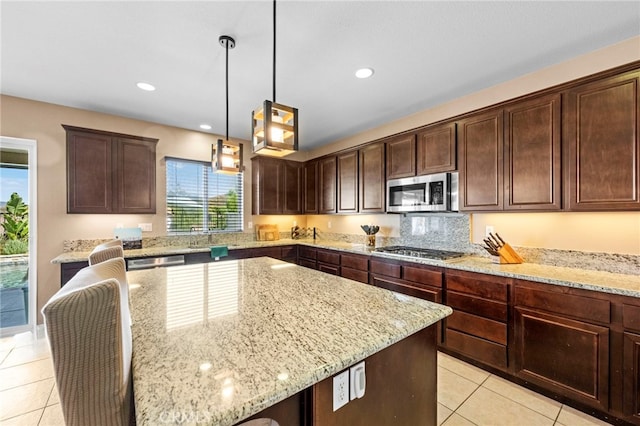 kitchen featuring decorative light fixtures, light stone counters, appliances with stainless steel finishes, and dark brown cabinets