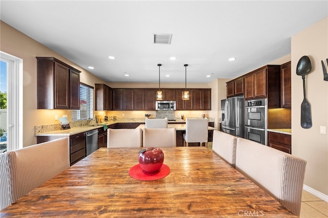 kitchen with decorative light fixtures, a kitchen island, dark brown cabinetry, appliances with stainless steel finishes, and light tile patterned floors