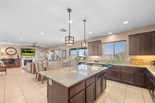 kitchen with light tile patterned floors, ceiling fan, decorative light fixtures, a kitchen island, and dark brown cabinetry