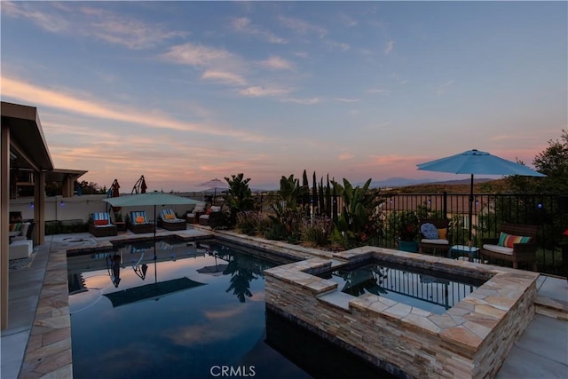 pool at dusk with a patio area and an in ground hot tub