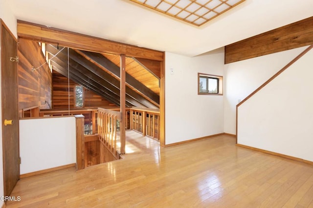 unfurnished living room featuring vaulted ceiling with beams, wood walls, a healthy amount of sunlight, and hardwood / wood-style flooring