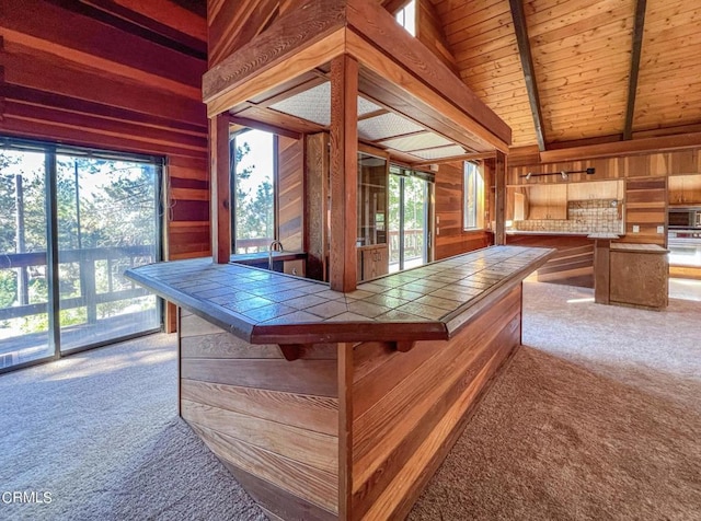 bar with a wealth of natural light, wood walls, tile counters, and light carpet