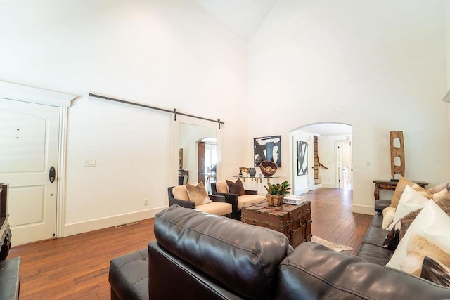 living room featuring a barn door, wood-type flooring, and high vaulted ceiling