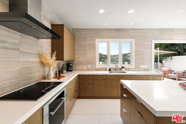 kitchen featuring black electric cooktop, oven, sink, wall chimney range hood, and light tile patterned floors