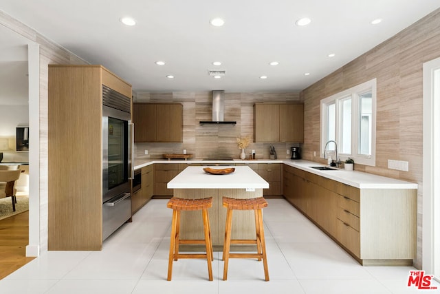 kitchen with wall chimney range hood, light tile patterned floors, sink, and a center island