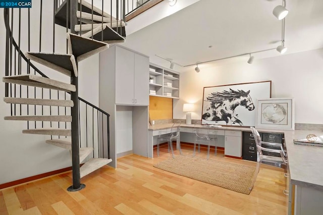 office with light wood-type flooring, built in desk, and rail lighting