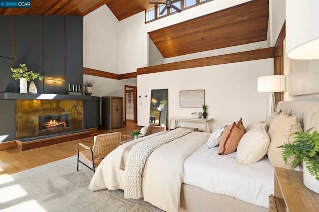 bedroom with a stone fireplace, high vaulted ceiling, wooden ceiling, and light wood-type flooring