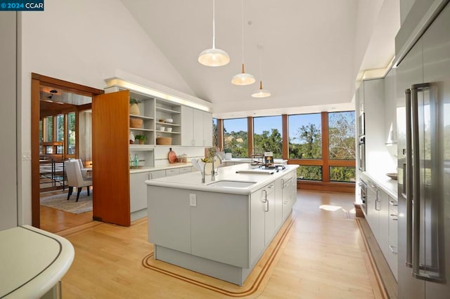 kitchen with sink, high vaulted ceiling, light hardwood / wood-style flooring, hanging light fixtures, and an island with sink