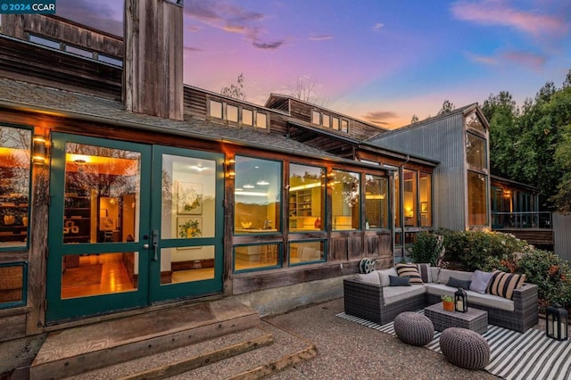 back house at dusk with outdoor lounge area, french doors, and a patio