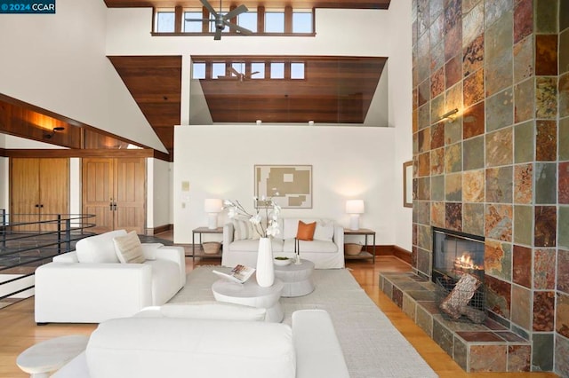 living room featuring hardwood / wood-style flooring, ceiling fan, a towering ceiling, and a tiled fireplace