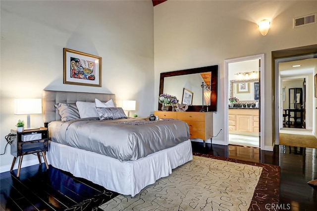 bedroom with hardwood / wood-style floors, a towering ceiling, and ensuite bath