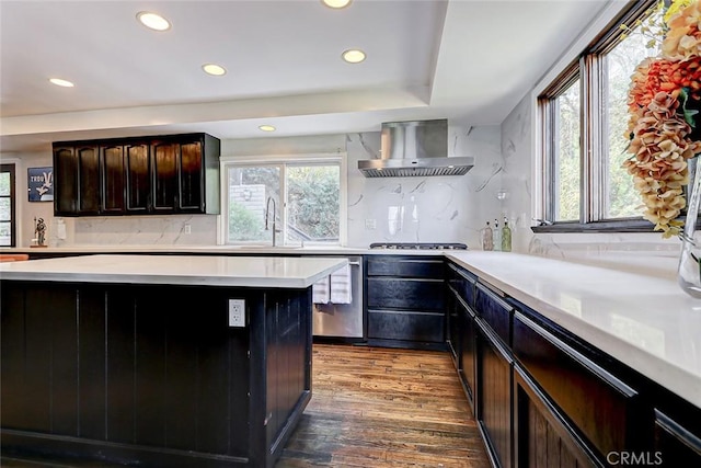 kitchen featuring backsplash, wall chimney exhaust hood, dark brown cabinets, sink, and wood-type flooring