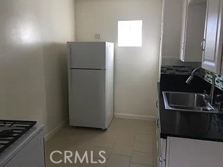 kitchen featuring light tile patterned floors, sink, white fridge, and white cabinetry