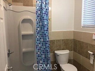 bathroom with tile walls, toilet, and a shower with shower curtain