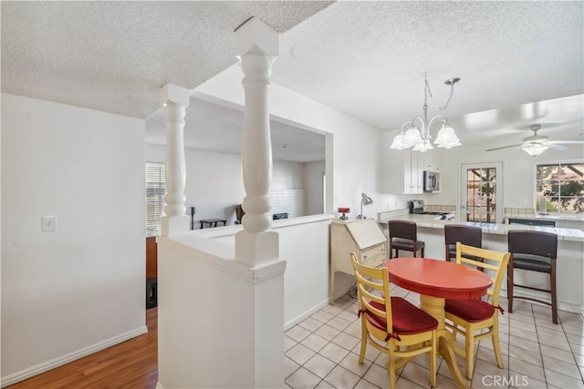 dining room with ceiling fan with notable chandelier, decorative columns, light tile patterned floors, and a textured ceiling