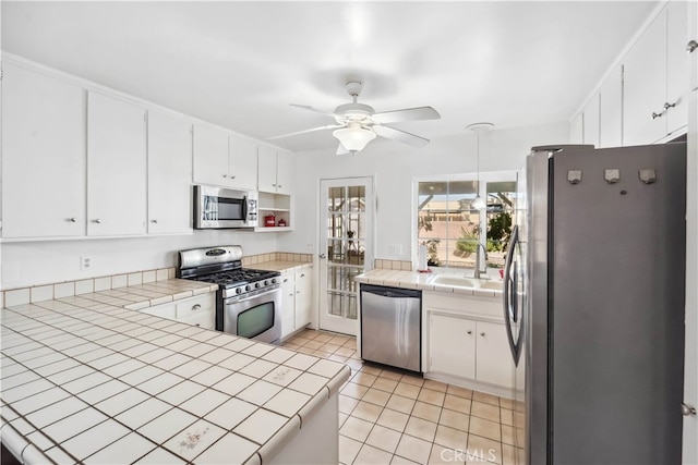 kitchen with sink, tile counters, white cabinets, appliances with stainless steel finishes, and light tile patterned floors