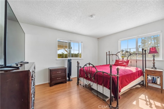 bedroom with light wood-type flooring, multiple windows, and a textured ceiling