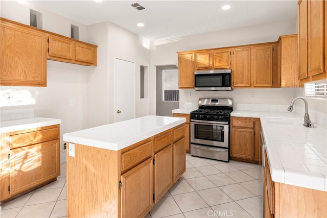 kitchen with light tile patterned flooring, sink, tile countertops, appliances with stainless steel finishes, and a center island