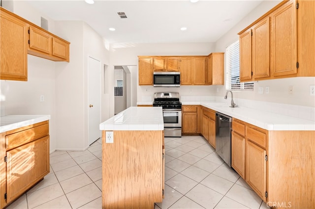 kitchen featuring sink, light tile patterned floors, a kitchen island, appliances with stainless steel finishes, and tile counters