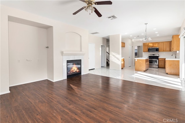 unfurnished living room with ceiling fan with notable chandelier, sink, light hardwood / wood-style flooring, and a tile fireplace