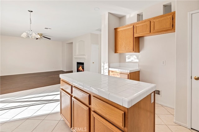 kitchen featuring decorative light fixtures, tile counters, a center island, ceiling fan with notable chandelier, and light hardwood / wood-style floors