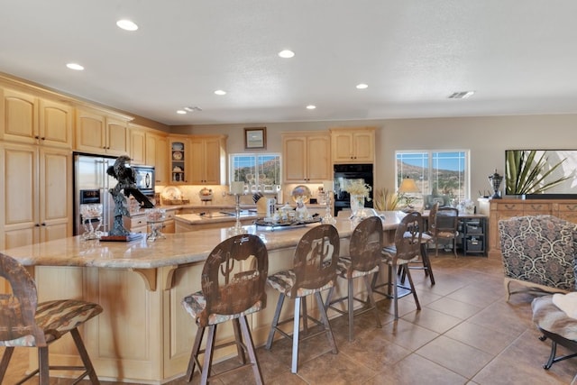 kitchen featuring light tile patterned flooring, light brown cabinetry, a kitchen breakfast bar, stainless steel appliances, and light stone countertops