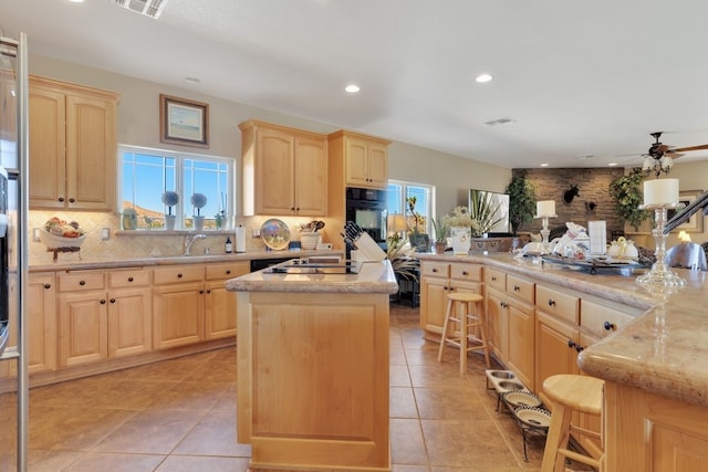 kitchen featuring light brown cabinetry, black appliances, a center island, and light tile patterned floors