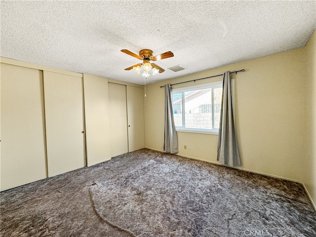 unfurnished bedroom featuring two closets, carpet flooring, a textured ceiling, and ceiling fan