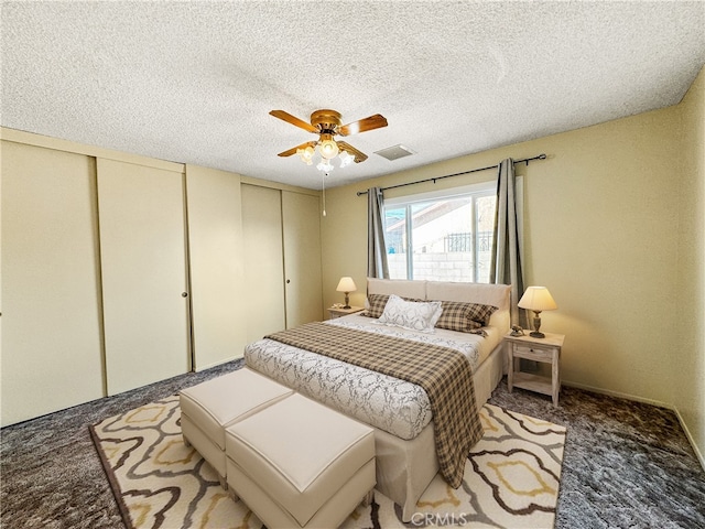 bedroom with carpet floors, two closets, a textured ceiling, and ceiling fan