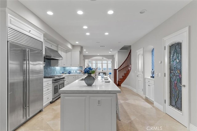 kitchen with white cabinetry, backsplash, wall chimney range hood, high end appliances, and a center island