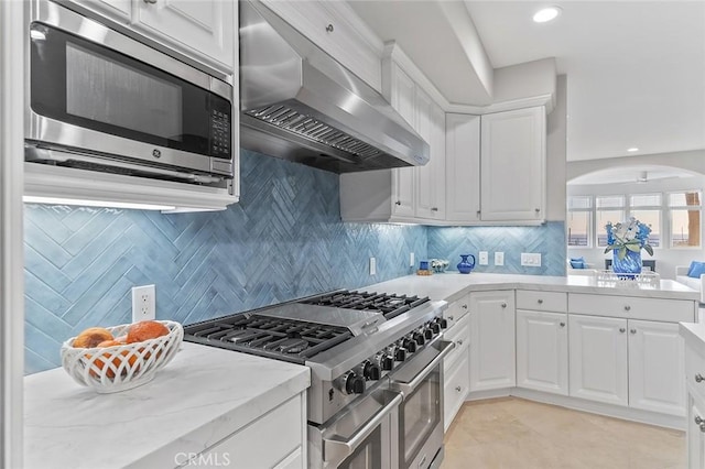 kitchen with light tile patterned floors, exhaust hood, appliances with stainless steel finishes, and white cabinetry