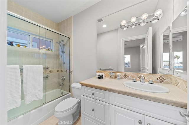 full bathroom featuring toilet, a healthy amount of sunlight, backsplash, vanity, and shower / bath combination with glass door