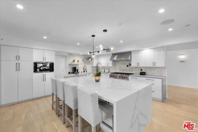 kitchen with a kitchen island, white cabinets, wall chimney range hood, and light wood-type flooring