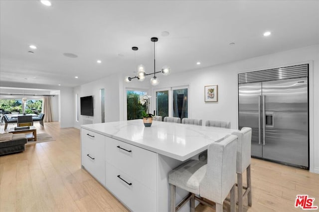 kitchen with a kitchen island, white cabinetry, light hardwood / wood-style floors, decorative light fixtures, and built in refrigerator