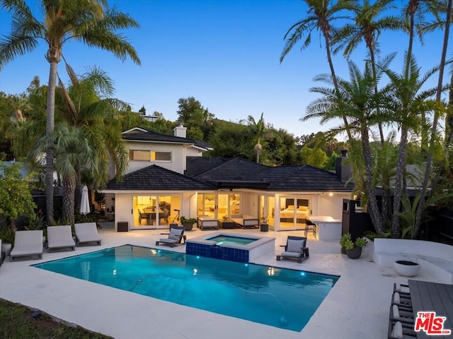 pool at dusk with a patio area and an in ground hot tub