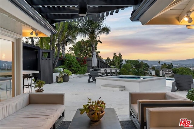 patio terrace at dusk with an in ground hot tub, a mountain view, ceiling fan, and outdoor lounge area