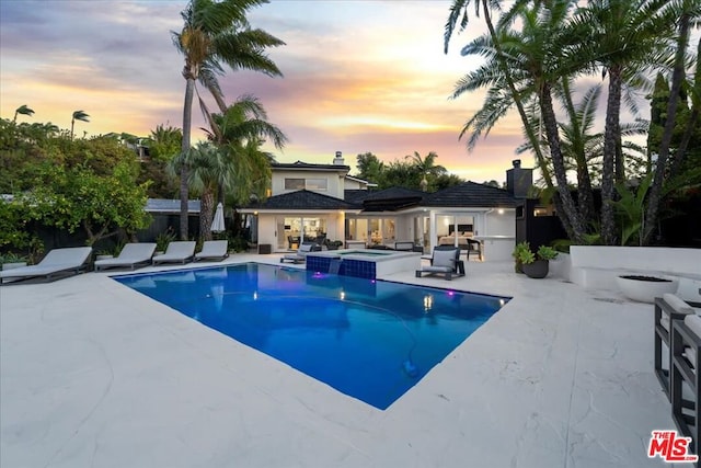 pool at dusk featuring a patio area and an outdoor hangout area