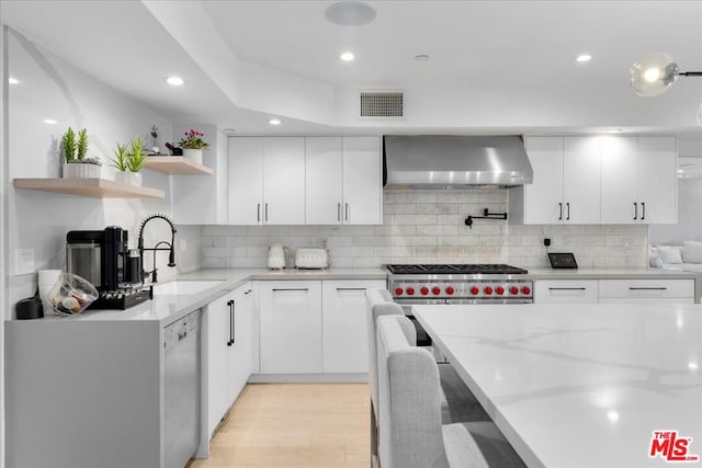 kitchen featuring white cabinets, light stone counters, light hardwood / wood-style floors, wall chimney exhaust hood, and sink