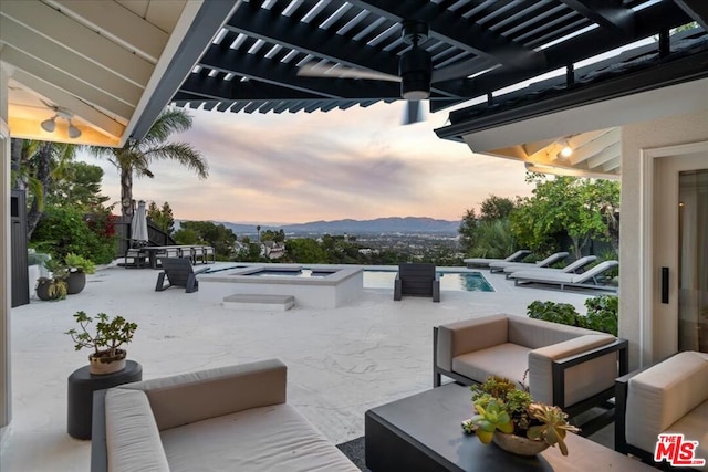 patio terrace at dusk with a swimming pool with hot tub, a mountain view, ceiling fan, and an outdoor hangout area