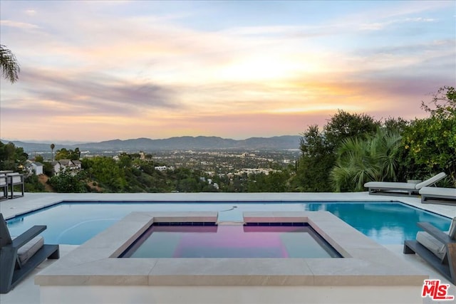 pool at dusk with a mountain view and an in ground hot tub