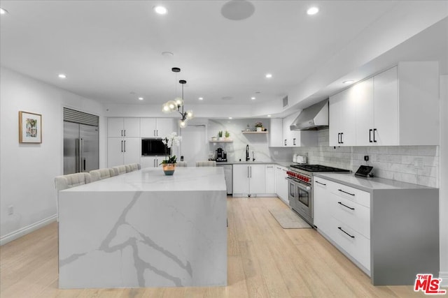 kitchen featuring a kitchen island, wall chimney range hood, high quality appliances, pendant lighting, and white cabinets